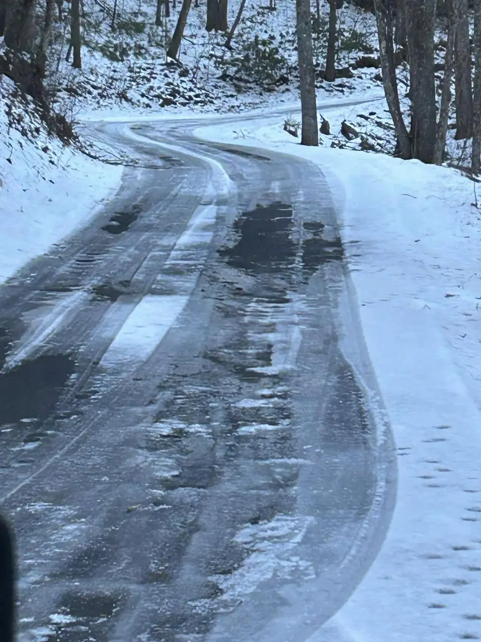 Winding mountain road packed with snow and ice through the trees